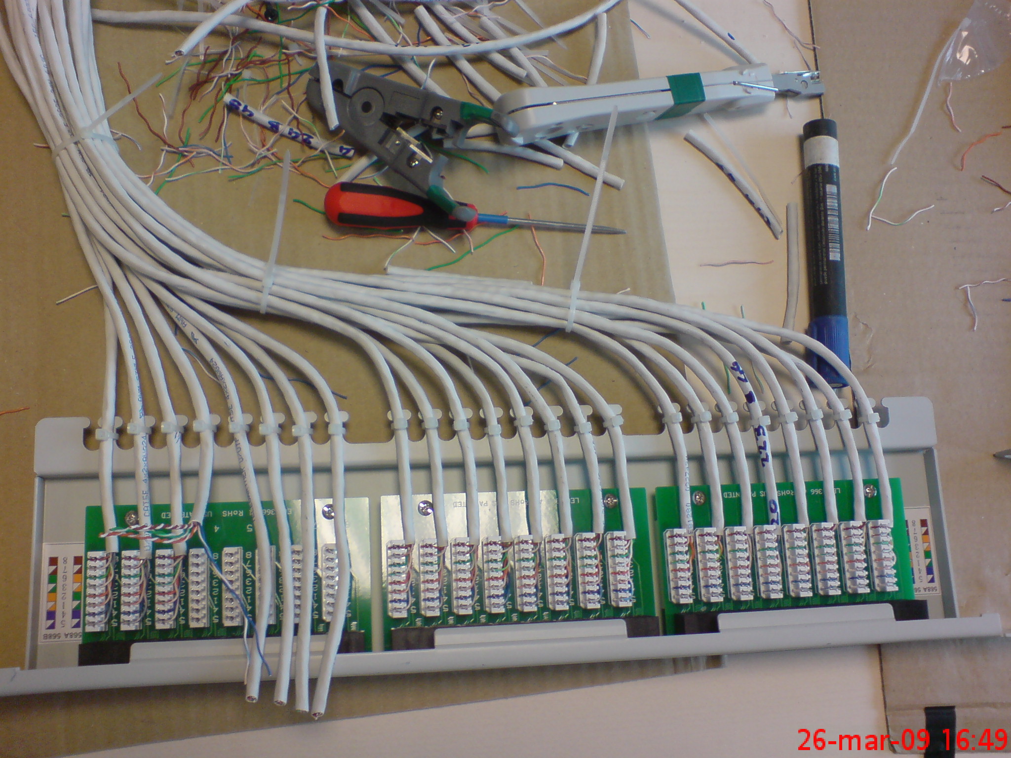 Panel krosowniczy z podłączonymi kablami sieciowymi, narzędzia do zarabiania kabli i marker na stole roboczym. Widoczne oznaczenia kolorystyczne na złączach.