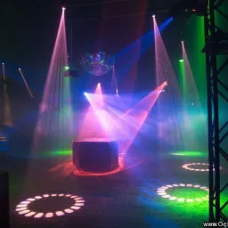 Scena oświetlona kolorowymi reflektorami, z kulą dyskotekową i podświetlonym podestem, przygotowana do występu, widoczna konstrukcja sceniczna po prawej.