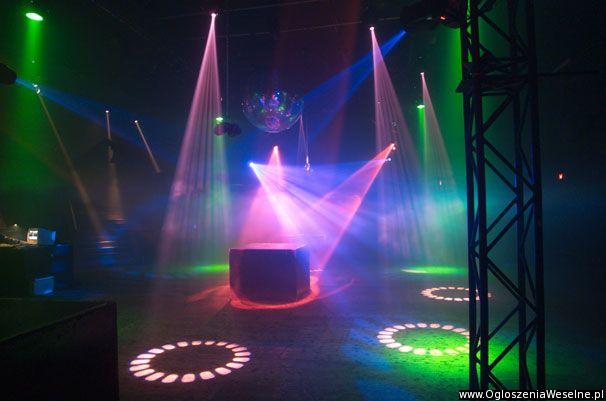 Scena oświetlona kolorowymi reflektorami, z kulą dyskotekową i podświetlonym podestem, przygotowana do występu, widoczna konstrukcja sceniczna po prawej.