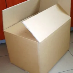 Otwarty karton klapowy, widoczne trzy warstwy tektury falistej od wewnątrz, na podłodze z płytek.