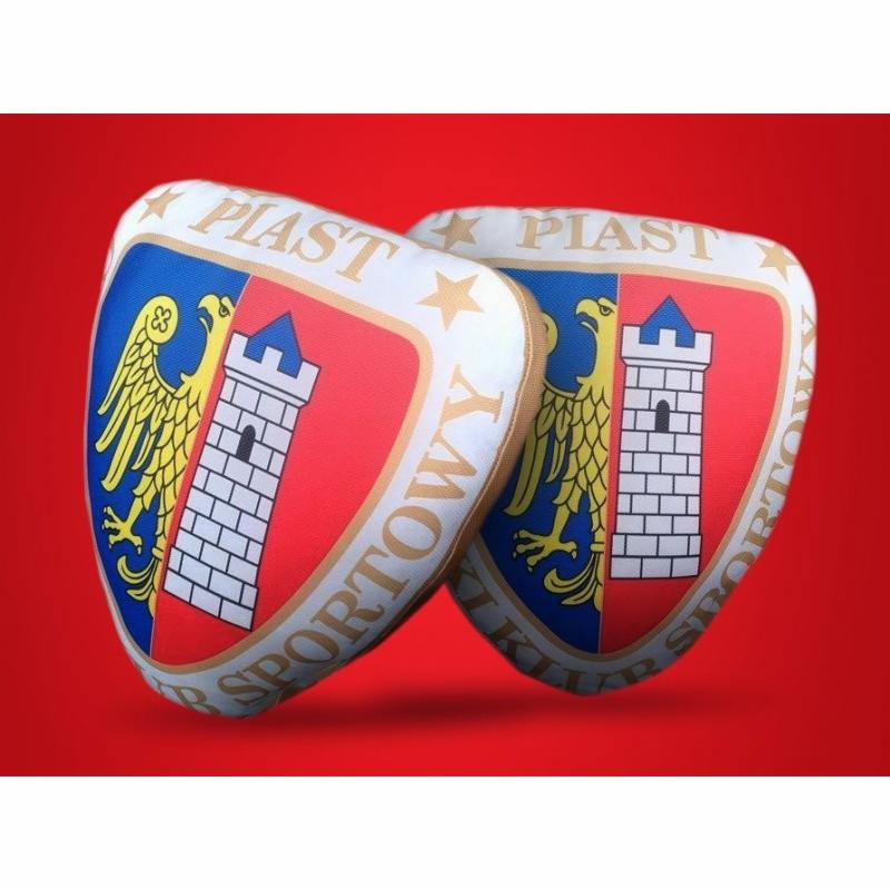 Dwie poduszki w kształcie herbu klubu sportowego Piast, z orłem i wieżą na czerwono-niebieskim tle, na jednolitym czerwonym tle.