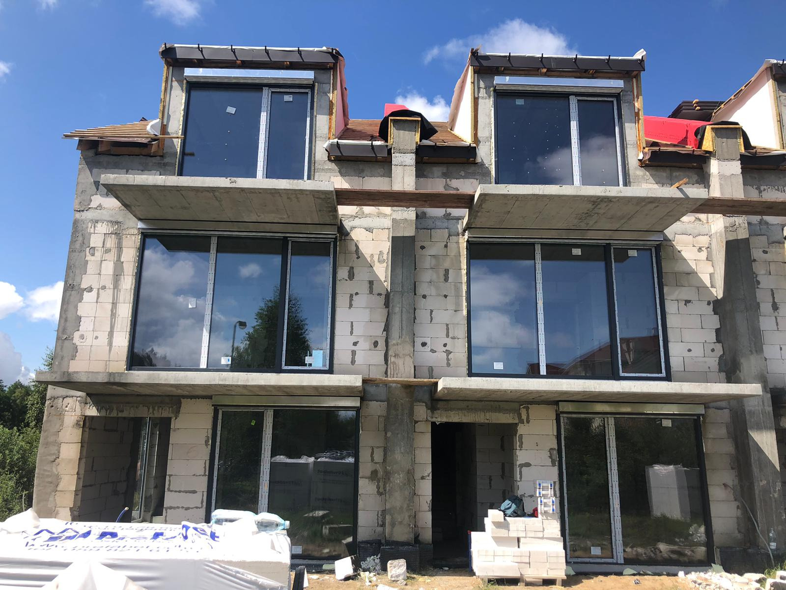 Montaż stolarki okiennej w Lubinie. Surowy stan budynku z dużymi oknami z czarnymi ramami, widoczne materiały budowlane. Nowoczesna architektura w trakcie realizacji.