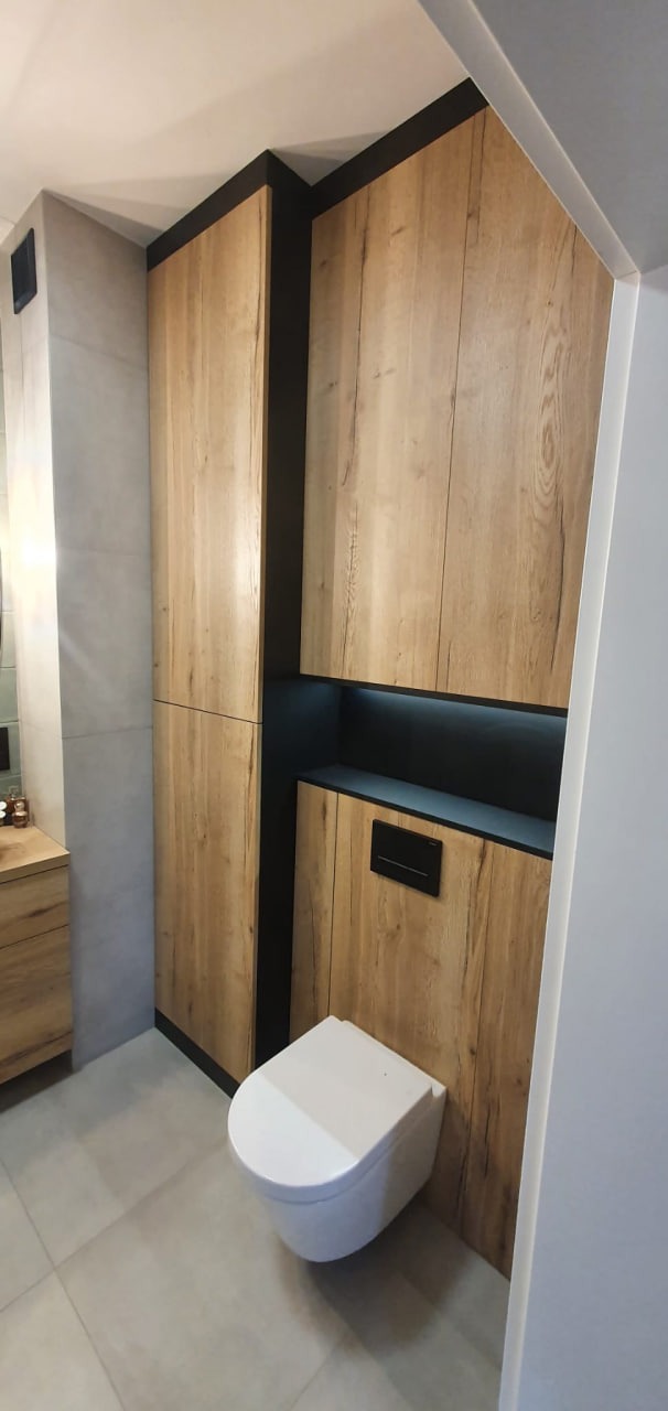 Nowoczesna toaleta podwieszana z zabudową z drewnopodobnych paneli w Twardogórze, z czarnymi akcentami i podświetleniem LED.