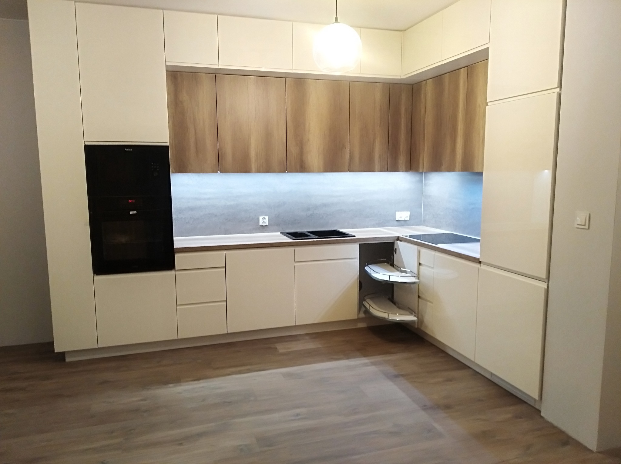 Jasna, nowoczesna kuchnia z drewnianymi frontami szafek górnych i białymi dolnymi, widoczny piekarnik w zabudowie i wysuwany narożny system półek.