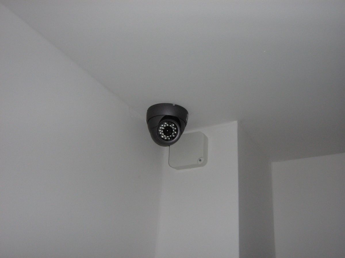 Kopułkowa kamera przemysłowa zamontowana na suficie w rogu pomieszczenia, obok widoczna puszka instalacyjna.