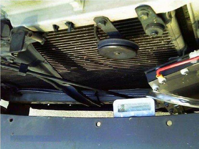 Widok na zamontowany generator HHO SLIMLINE 5.0 - DRY CELL w komorze silnika samochodu, widoczny radiator, przewody i wyświetlacz urządzenia.