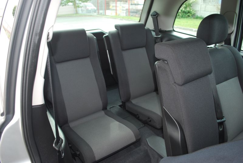 Wnętrze samochodu z trzema rzędami siedzeń, szaro-czarna tapicerka, widok na rozłożone fotele w drugim i trzecim rzędzie.