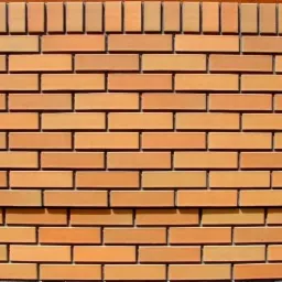 Fragment ściany z cegły klinkierowej w odcieniach pomarańczy, z dekoracyjnym wykończeniem górnej krawędzi w postaci pionowo ułożonych cegiełek.