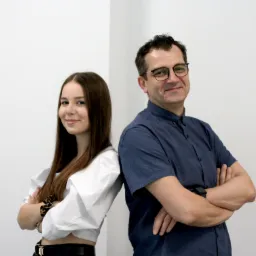 Portret dwójki pracowników biura w Sępólnie Krajeńskim, opartych plecami o ścianę, z założonymi rękami i uśmiechem.