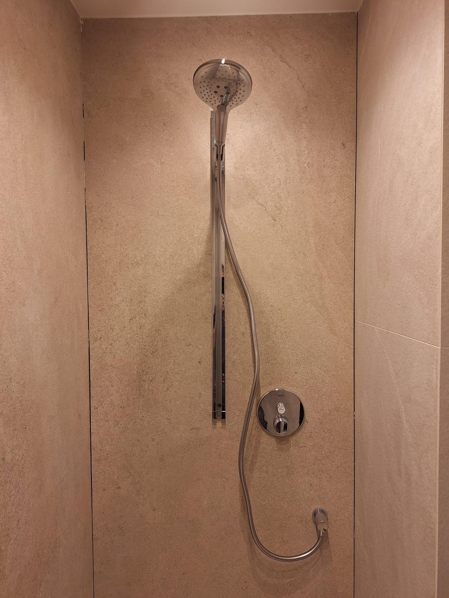 Zamontowany zestaw prysznicowy Grohe z deszczownicą na ścianie wyłożonej płytkami w odcieniach beżu i brązu.