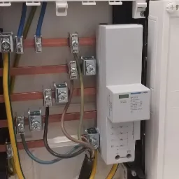 Wnętrze białej skrzynki elektrycznej z zamontowanym ogranicznikiem przepięć Hager SPA301Z, widoczne miedziane szyny z podłączonymi przewodami o różnych kolorach i przekrojach.