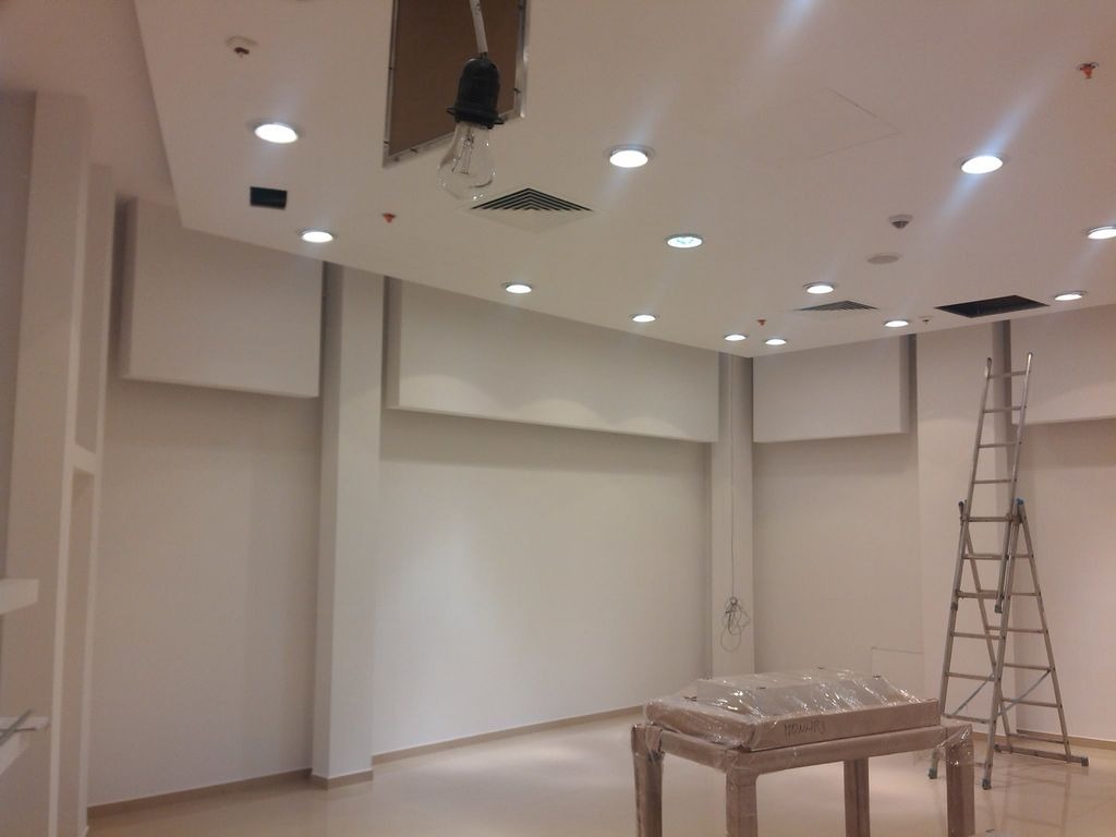 Wnętrze sklepu w trakcie montażu oświetlenia sufitowego, widoczna drabina i tymczasowa żarówka zwisająca z otworu w suficie.