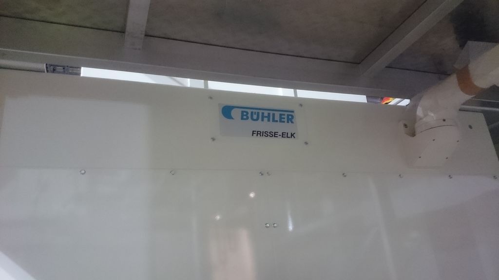 Biała obudowa urządzenia z logo Bühler Frisse-Elk, widoczna instalacja wentylacyjna z białych rur PCV pod sufitem.