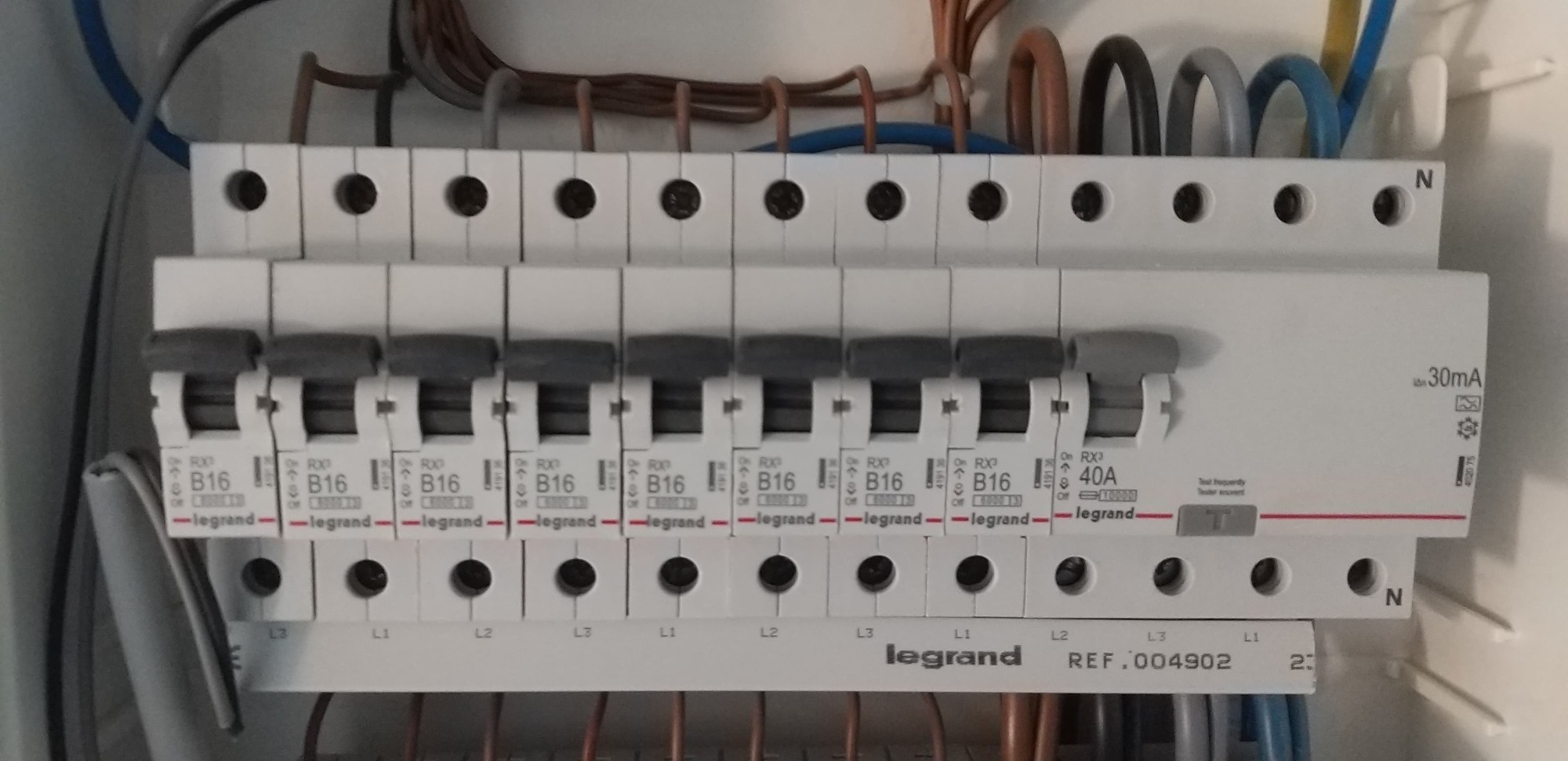 Szczegółowe ujęcie rozdzielnicy elektrycznej marki Legrand z widocznymi bezpiecznikami B16 i jednym 40A, przewody w górnej i dolnej części kadru, oznaczenia L1, L2, L3.