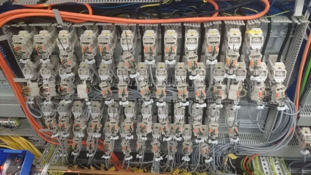 Rozbudowana szafa sterownicza z licznymi modułami elektrycznymi, okablowaniem w peszlach i listwach, widok z bliska na połączenia i złączki.