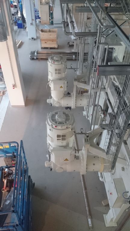 Widok z góry na zainstalowany system rur i silników elektrycznych w hali przemysłowej, z widocznym podnośnikiem koszowym w lewym dolnym rogu.