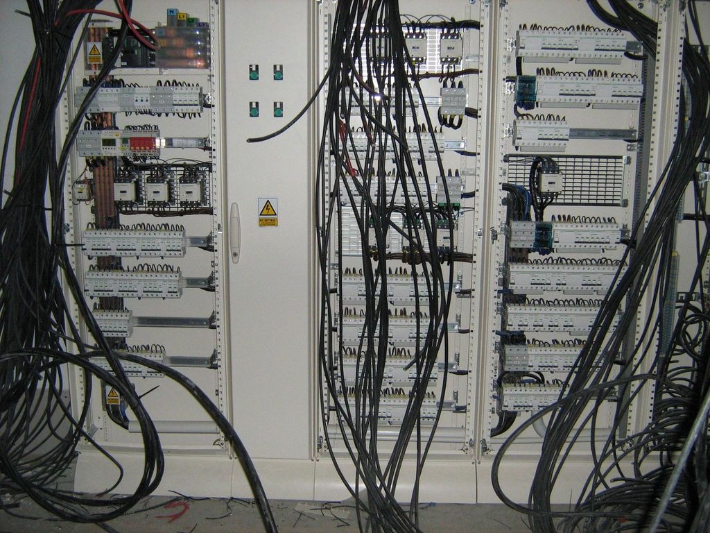 Rozdzielnica elektryczna z licznymi przewodami w trakcie montażu, widoczne zabezpieczenia i listwy zaciskowe, okablowanie w nieładzie.