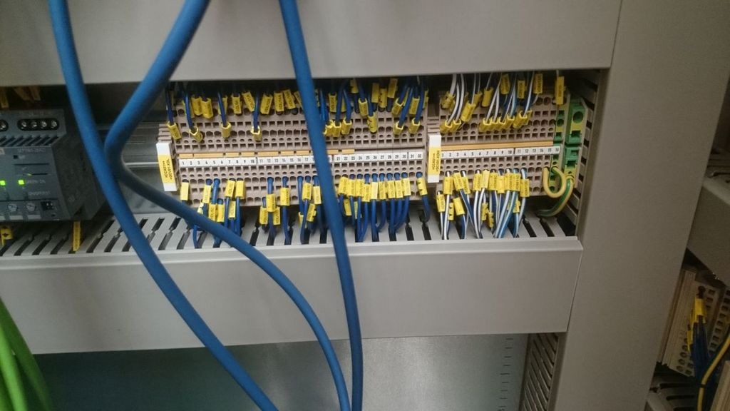 Szczegółowe ujęcie szafy sterowniczej z licznymi przewodami oznaczonymi żółtymi etykietami, podłączonymi do listew zaciskowych, widoczne także elementy automatyki przemysłowej Siemens.