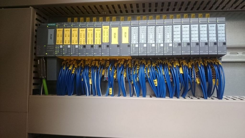 Panel sterowania Siemens Simatic S7-200SP z modułami wejść/wyjść, okablowanie w niebieskich przewodach z żółtymi oznaczeniami, widok z bliska na szafę sterowniczą.