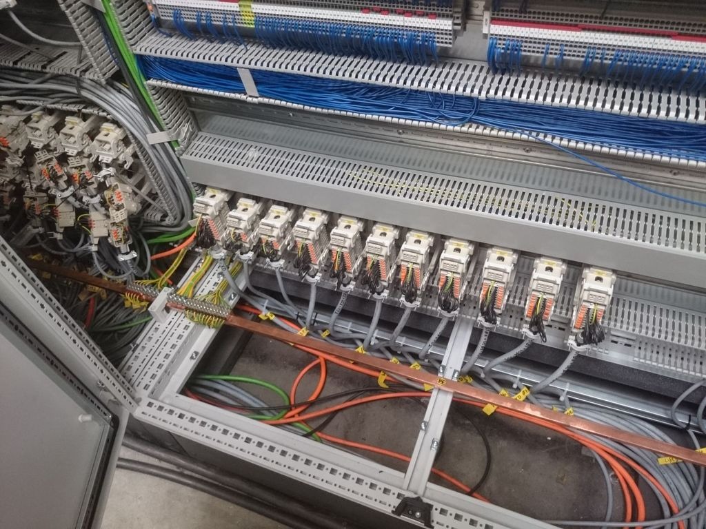 Wnętrze szafy sterowniczej z licznymi przewodami, złączkami i szynami montażowymi, widok z otwartymi drzwiami szafy.