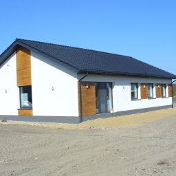 Agencja Budowlana WITAND - Nowoczesny dom jednorodzinny z czarnym dachem w Łodzi. Elewacja biała z drewnianymi akcentami. Widoczne okna i drzwi balkonowe. Teren wokół domu przygotowany pod trawnik.