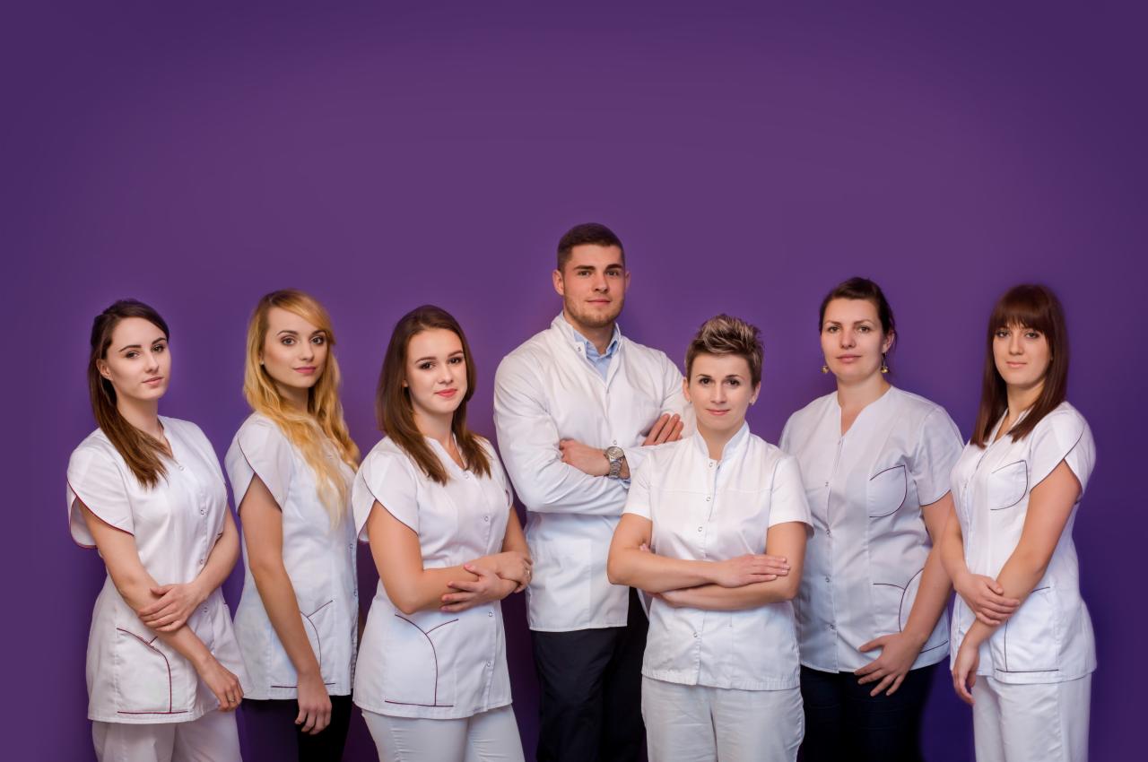 Grupa siedmiu osób w białych uniformach pozuje na tle fioletowej ściany, prezentując zespół profesjonalistów.