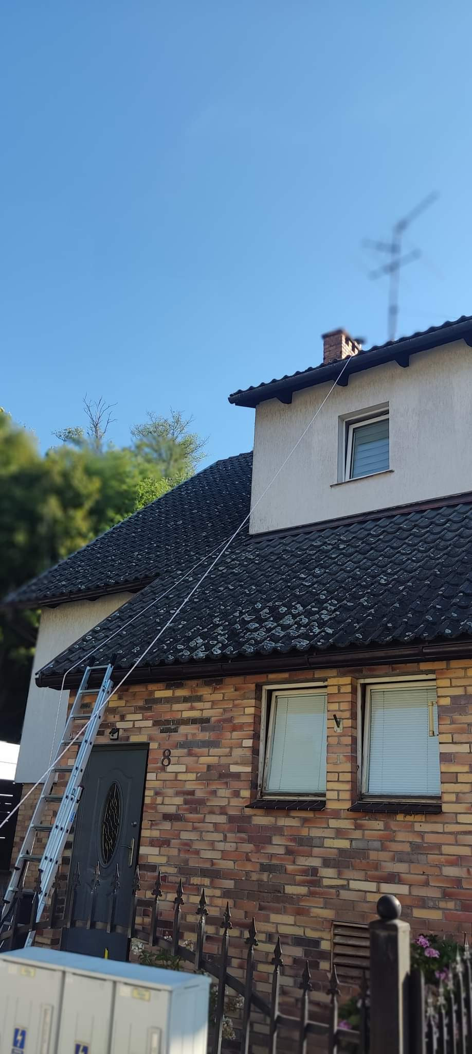 Dwupiętrowy dom z cegły z aluminiową drabiną opartą o rynnę i dach pokryty mchem.