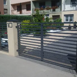 Nowoczesna, grafitowa brama wjazdowa z poziomymi szczeblami, zamontowana na beżowych słupkach z numerem '10'. Tło: budynki mieszkalne i zadbana zieleń.