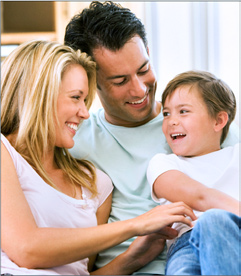 Uśmiechnięta rodzina z Wrocławia: mama, tata i syn, siedząca na kanapie w jasnym wnętrzu. Syn patrzy z radością na ojca.