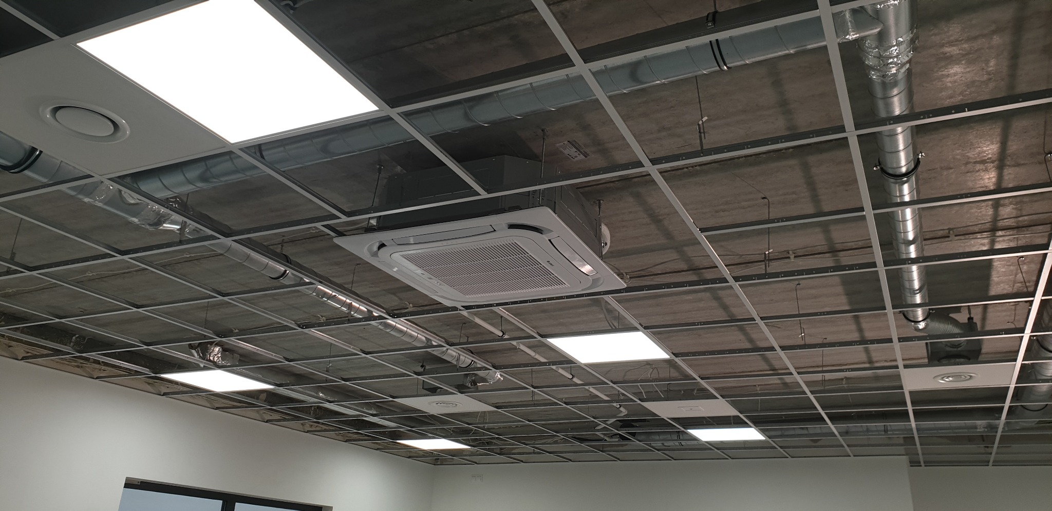 Zamontowany kasetonowy klimatyzator GREE w suficie podwieszanym rastrowym, widoczne instalacje wentylacyjne i oświetlenie LED.