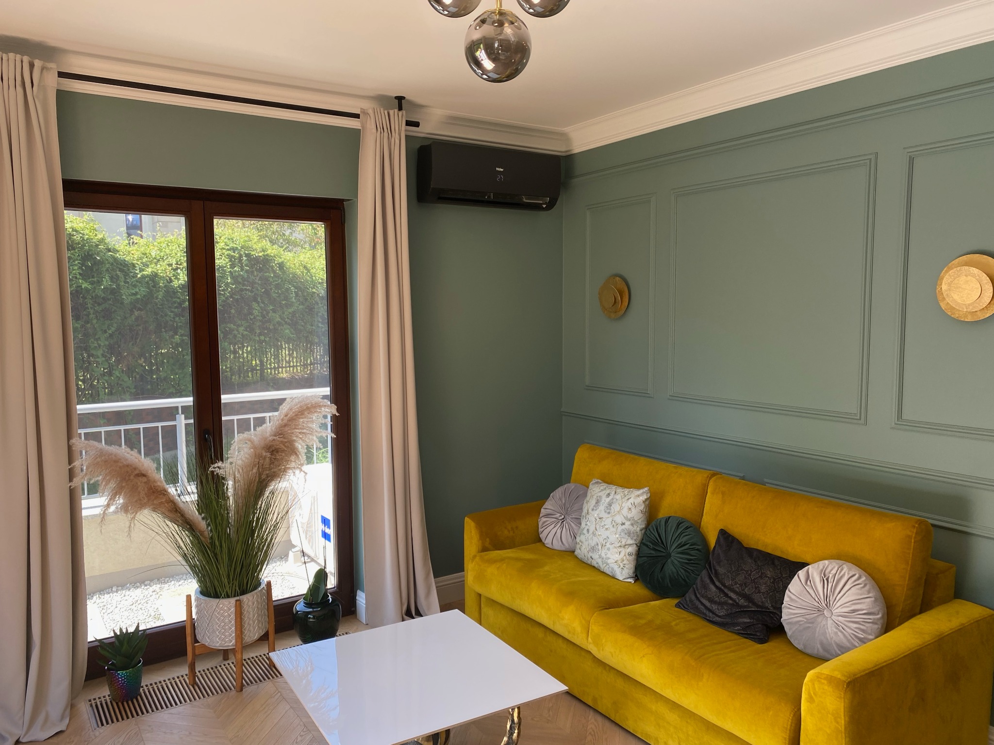 Czarny klimatyzator HAIER FLEXIS Black Matt zamontowany na ścianie w salonie z zielonymi panelami, żółtą sofą i dekoracjami.