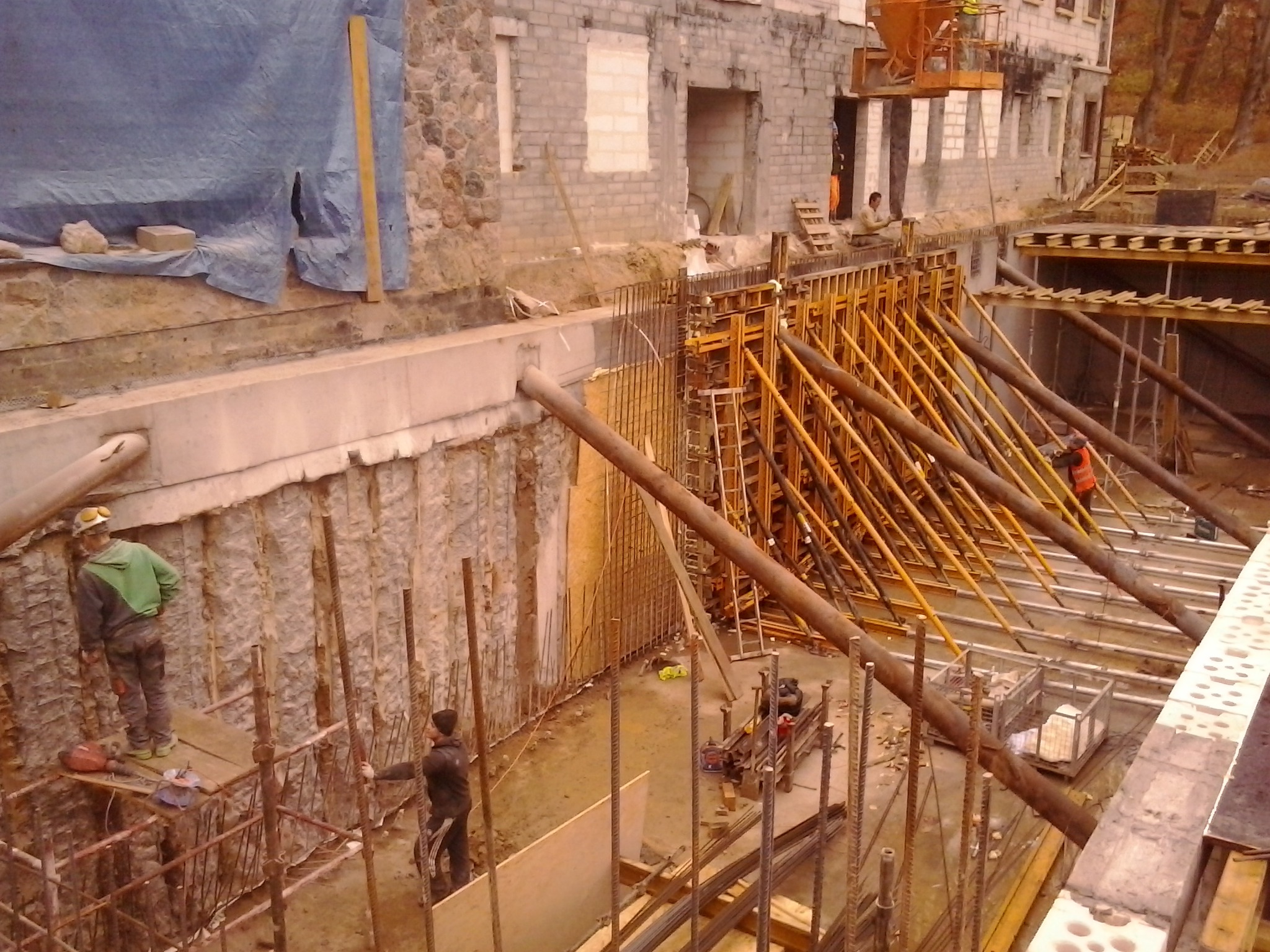 Budowa fundamentów budynku wielorodzinnego, widoczne szalunki, zbrojenia, pracownicy w trakcie robót ziemnych i betonowania.
