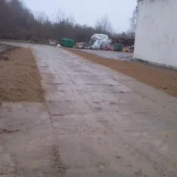 Ułożone płyty betonowe i obsypana ziemią krawędź terenu w Szczecinie. Przygotowanie podłoża pod budowę lub utwardzenie terenu. Widoczne materiały budowlane w tle.