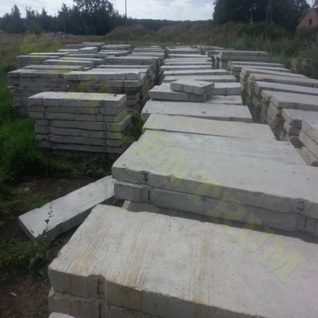 Stosy prefabrykowanych płyt betonowych na trawiastym terenie, gotowe do użycia w budownictwie lub jako elementy nawierzchni. Widok z bliska na teksturę betonu.