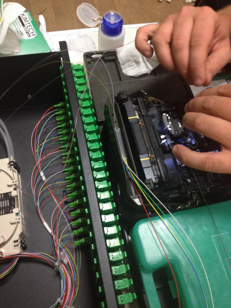 Technik łączy światłowody za pomocą spawarki światłowodowej, widoczna kaseta z adapterami światłowodowymi i kable patchcord.