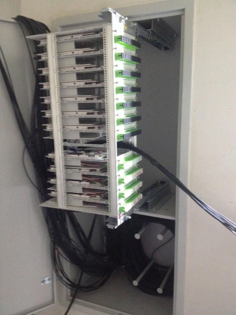 Szafa telekomunikacyjna z panelami krosowniczymi, widoczne liczne kable światłowodowe wchodzące do szafy.