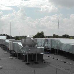 Krystwik wentylacja klimatyzacja - System kanałów wentylacyjnych z metalu na dachu budynku, widoczne elementy rekuperacji i odgromniki na tle pochmurnego nieba.