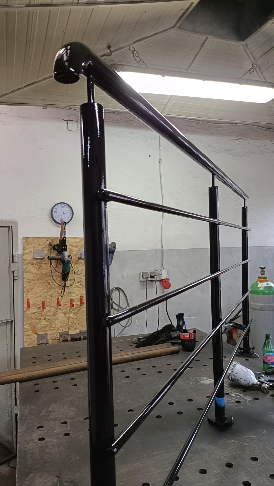 W trakcie produkcji: czarna, metalowa balustrada z czterema poprzeczkami, spawana na stole warsztatowym z widocznymi narzędziami i butlą z gazem w tle.