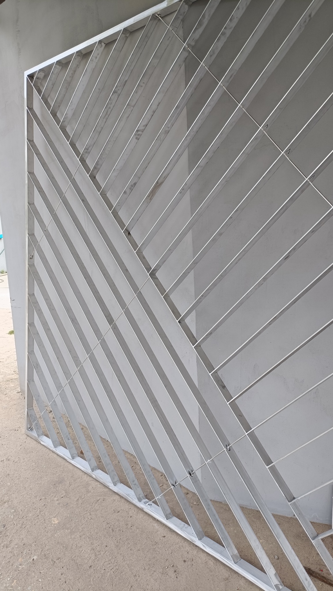 Nowoczesna, surowa brama z ukośnymi, metalowymi profilami, widoczna z bliska, z elementami mocującymi na dole.