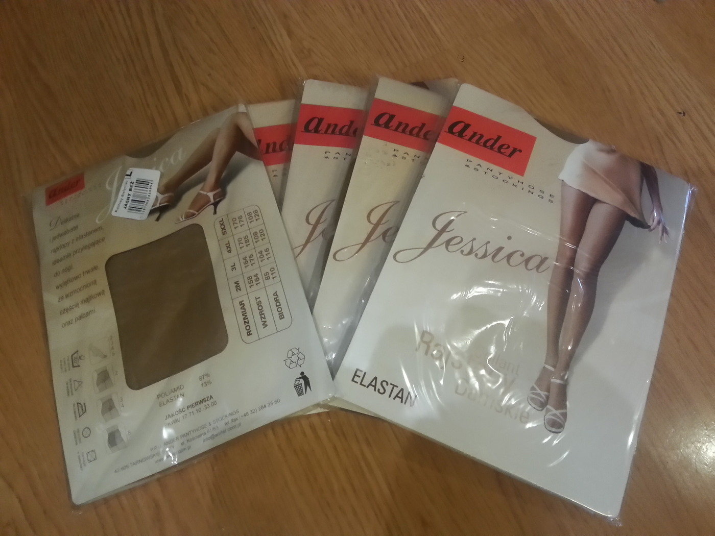 Kilka opakowań rajstop damskich marki Ander Jessica leżących na drewnianej powierzchni, widoczne opakowania z informacjami o rozmiarach i składzie, jedno z opakowań z brązowym materiałem rajstop...