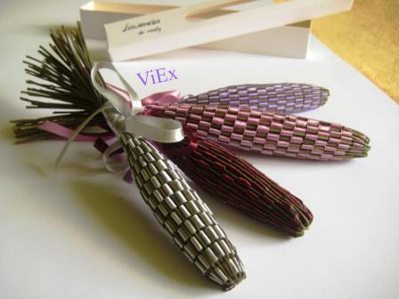 Ręcznie robione woreczki zapachowe z lawendy w trzech kolorach (srebrny, różowy, fioletowy) z ozdobnymi wstążkami, leżące obok otwartego pudełka.