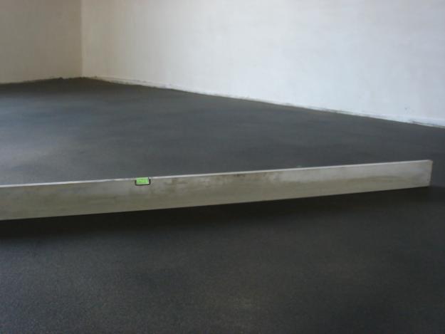 Świeżo wylana, ciemna posadzka wyrównywana długą poziomicą w jasnym pomieszczeniu.