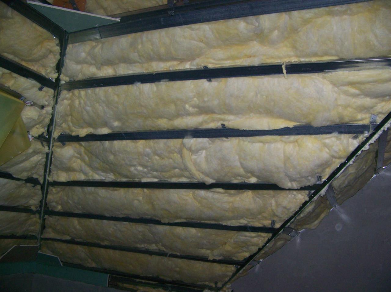 Izolacja poddasza wełną mineralną, widoczne metalowe profile konstrukcyjne i fragment płyty kartonowo-gipsowej.