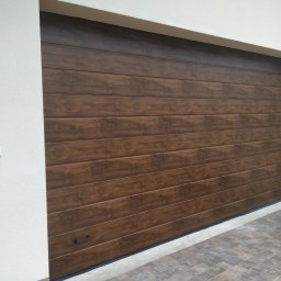 Mariusz Soszyński Przedsiębiorstwo Handlowo Usługowe - Zamknięta, segmentowa brama garażowa w kolorze ciemnego drewna z poziomymi panelami, zamontowana w jasnym garażu, widoczny fragment kostki brukowej i samochodu.