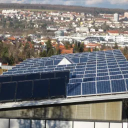 Instalacja fotowoltaiczna i kolektory słoneczne na dachu budynku z widokiem na miasto w tle, ujęcie z dołu, słoneczny dzień.