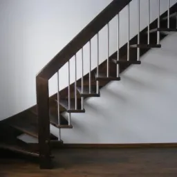 Ciemnobrązowe schody drewniane z metalowymi balustradami na białym tle ściany, widok z dołu.