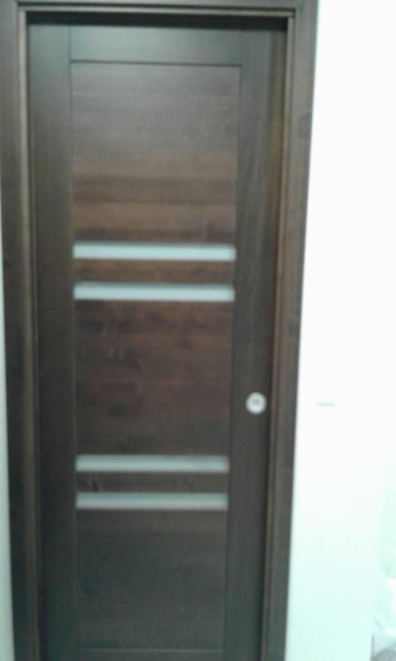 Ciemnobrązowe drzwi wewnętrzne z trzema poziomymi przeszkleniami, widoczna klamka, ościeżnica w kolorze drzwi.