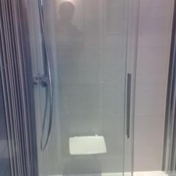 Uslugi glazurnicze - Nowoczesna kabina prysznicowa z siedziskiem, chromowaną armaturą i przesuwnymi drzwiami, wykończona jasnymi płytkami. Minimalistyczny design.