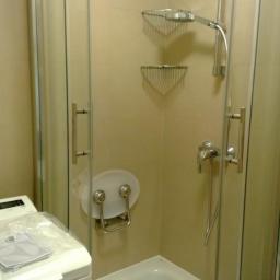 Uslugi glazurnicze - Nowoczesna kabina prysznicowa z siedziskiem i półkami w jasnej łazience. Widoczna pralka z dokumentacją. Minimalistyczny design, praktyczne rozwiązania.