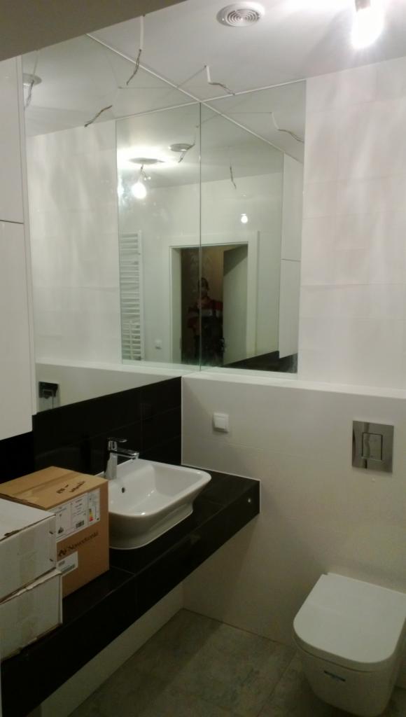 Nowoczesna łazienka z lustrem w mozaikę i czarnym blatem we Wrocławiu. Białe płytki i armatura tworzą minimalistyczny design. Widoczne elementy instalacji.